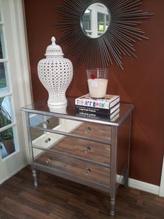 a mirrored table with a vase and books on it in front of a mirror that has a sunburst above it