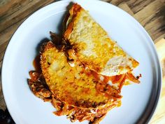 a white plate topped with lasagna covered in cheese and sauce on top of a wooden table