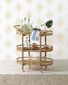 a bamboo bar cart with drinks on it in front of a wallpapered background