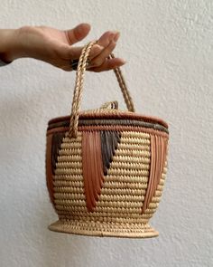 a hand holding a woven basket hanging from a rope on the wall with white walls in the background