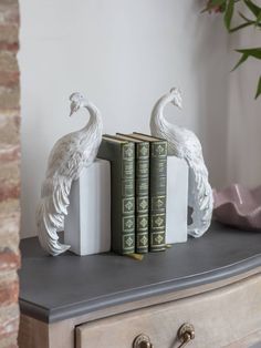 two books are sitting on a table next to a pair of white peacock figurines