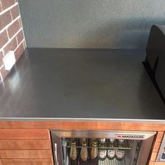 an open refrigerator with beer bottles in it next to a brick wall and counter top