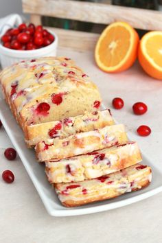 sliced oranges and cranberries on a white plate next to some bread with icing