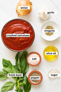 the ingredients to make homemade tomato sauce on a white countertop with basil leaves, garlic, onion, and other spices