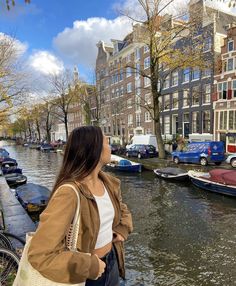 a woman standing on the edge of a canal with boats in the water behind her