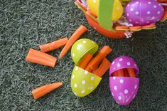 an assortment of colorful plastic easter eggs and carrots in a basket on the grass