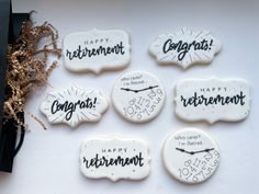 six decorated cookies with happy retirement written on the front and back, sitting next to some dried flowers