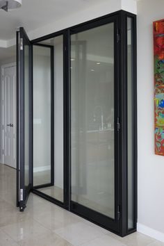 an empty room with black glass doors and paintings on the wall behind it, in front of a white tiled floor