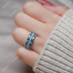 a woman's hand holding a ring with blue stones on it, in the middle of her fingers