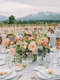 the table is set with white plates and silverware, pink flowers, and greenery