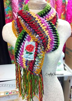 a white mannequin wearing a multicolored crocheted scarf with roses on it