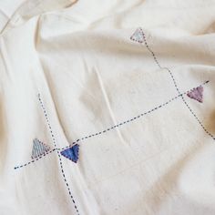 an embroidered piece of cloth on top of a white sheet with blue and red stitching