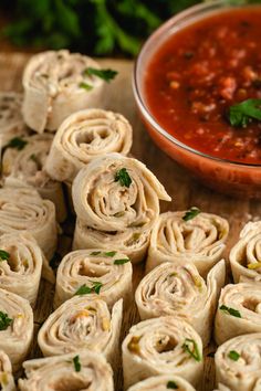 several rolled up food items on a cutting board next to a bowl of tomato sauce