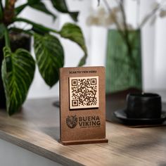 a wooden block with a qr code on it sitting on a table next to a potted plant