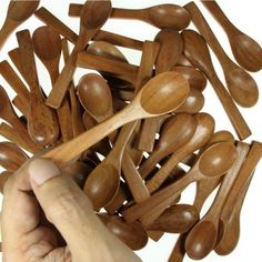 wooden spoons are being held by a person's hand over a pile of wood spoons