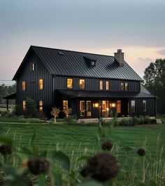 a large black house sitting on top of a lush green field next to tall grass