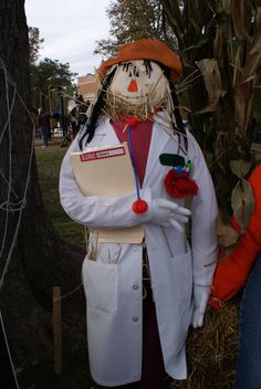 a scarecrow dressed in a lab coat and holding a clipboard next to a tree