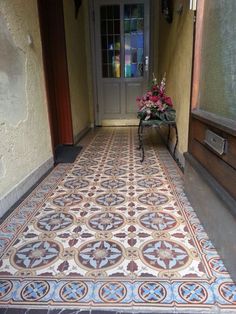 an ornate tile floor in front of a door with flowers on the table and potted plants