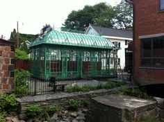 a green building with a glass roof in the middle of a yard next to brick buildings