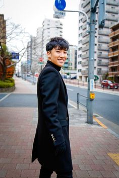 a young man standing on the side of a road next to a street light and buildings