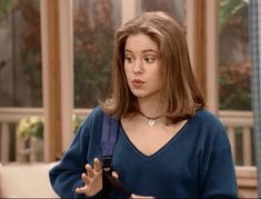 a woman holding a cell phone in her right hand and wearing a blue sweater on the other