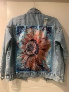 a denim jacket hanging on the wall with an image of a sunflower painted on it