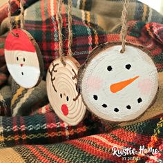 three wooden ornaments hanging from strings on a plaid blanket with snowman and reindeer faces