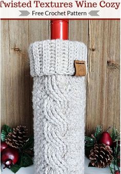 a white knitted wine bottle cover with a wooden background and pine cones around it