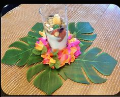 an arrangement of flowers, leaves and rocks in a glass on top of a table