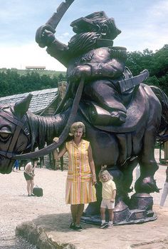 a woman and child standing next to a statue of an elephant with a man on it's back