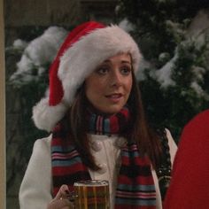 a woman wearing a santa hat and scarf holding a beer in front of a christmas tree