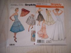 two paper dolls in dresses on a table next to each other, one is wearing a hat and the other has a dress