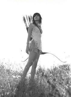 black and white photograph of a woman with arrows in her hands standing in a field