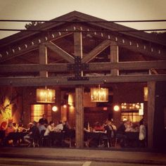 a group of people sitting at tables in front of a building with lights on it