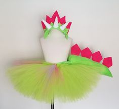 a green tutu skirt with pink and white spikes on it's head, sitting next to a mannequin