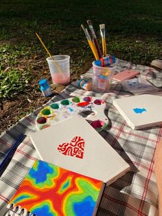 some art supplies are sitting on a plaid tablecloth with watercolor paints and brushes