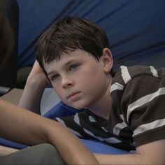 a young boy sitting in a chair with his hand on his head