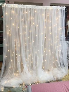 a white curtain with fairy lights hanging from it's sides in front of a bed