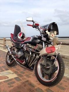 a red and black motorcycle parked on top of a brick road next to the ocean