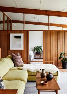 a living room filled with furniture and wooden paneling on the walls, along with potted plants