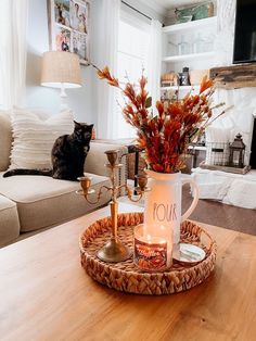 a cat sitting on a table next to a coffee cup and candle holder with flowers in it