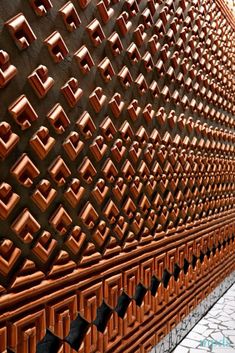 a wall made out of copper colored bricks and metal grates on the side of a building