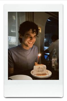 a man sitting in front of a cake with a lit candle on top of it