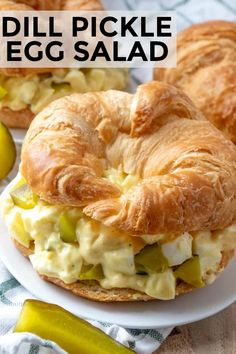 an egg salad sandwich on a croissant bun with pickle slices in the background