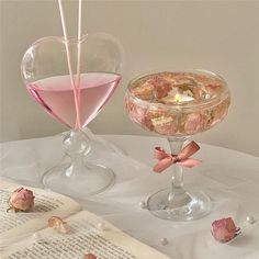 two glasses filled with pink liquid sitting on top of a table next to an open book