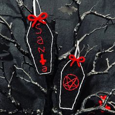 two black and red tags hanging from tree branches with bats on them, one has a pentagram attached to it