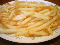 french fries on a white plate sitting on a wooden table