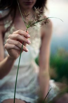 a woman sitting on the ground holding a flower in her hand and looking at it