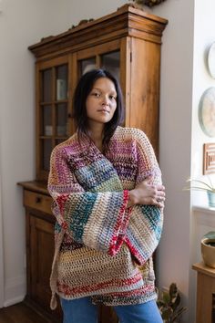 a woman standing in front of a wooden cabinet with her arms crossed and looking off to the side