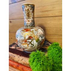 a vase sitting on top of a wooden table next to green moss covered plants and wood planks